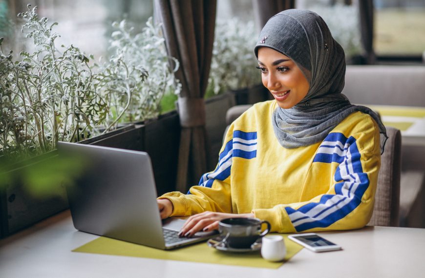 Pakistani woman in hijab inside a cafe working on laptop