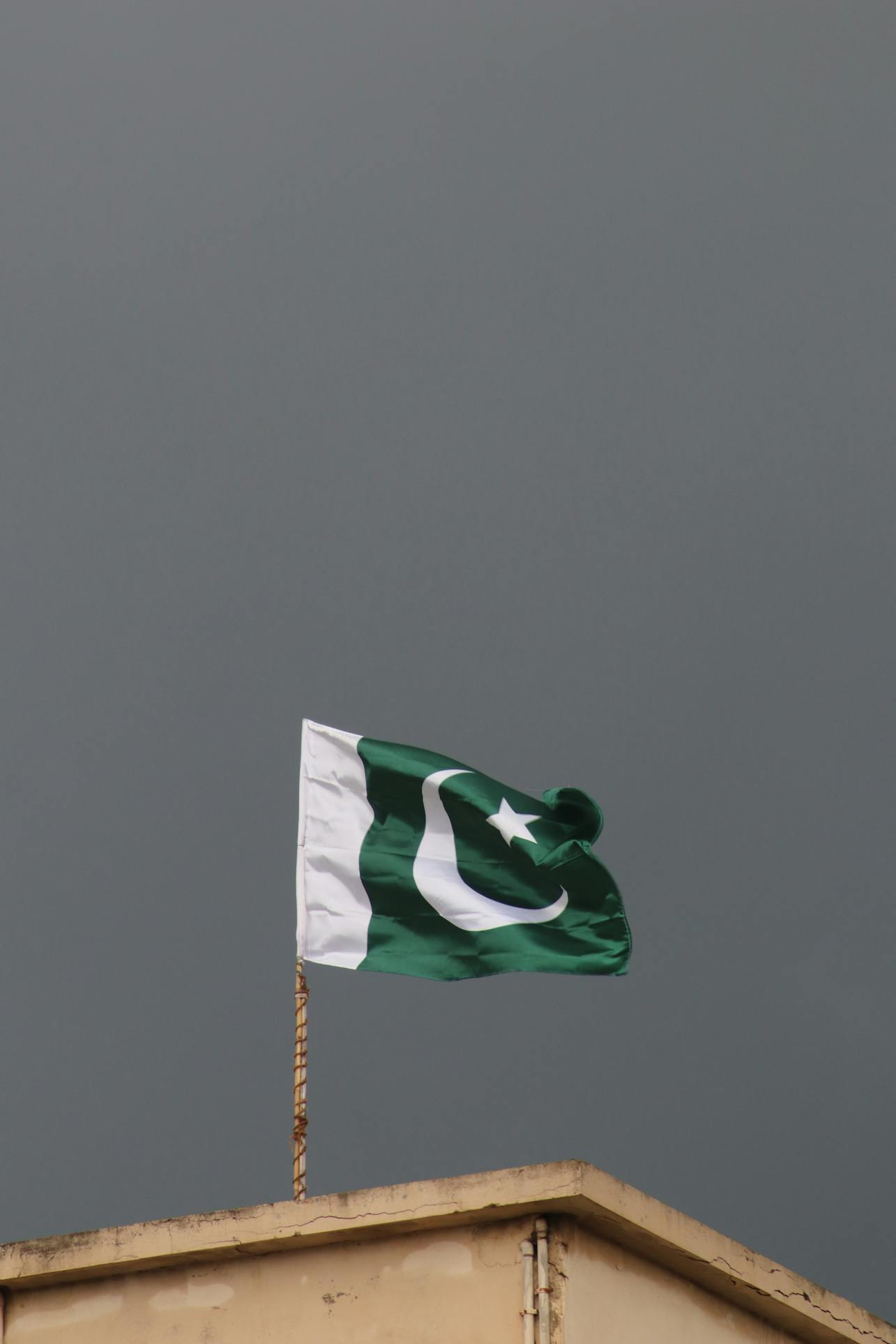The national flag of Pakistan waves prominently against a dark, stormy sky, symbolizing resilience. Truehost pakistan is now offering cheap .pk domains